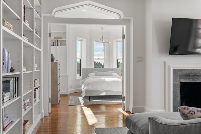 bedroom with a premium fireplace, baseboards, an inviting chandelier, and wood finished floors