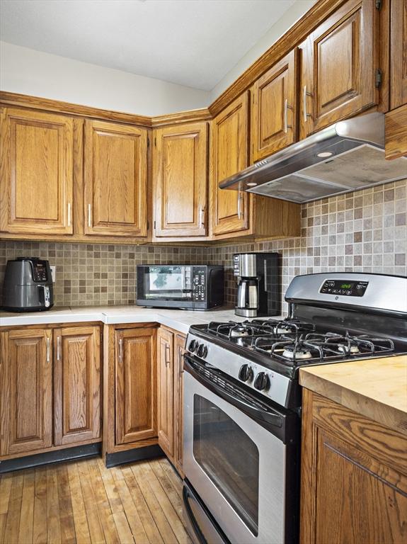537 Milk St, Fitchburg, MA 01420 - kitchen featuring stainless steel gas range, under cabinet range hood, light countertops, black microwave, and brown cabinetry