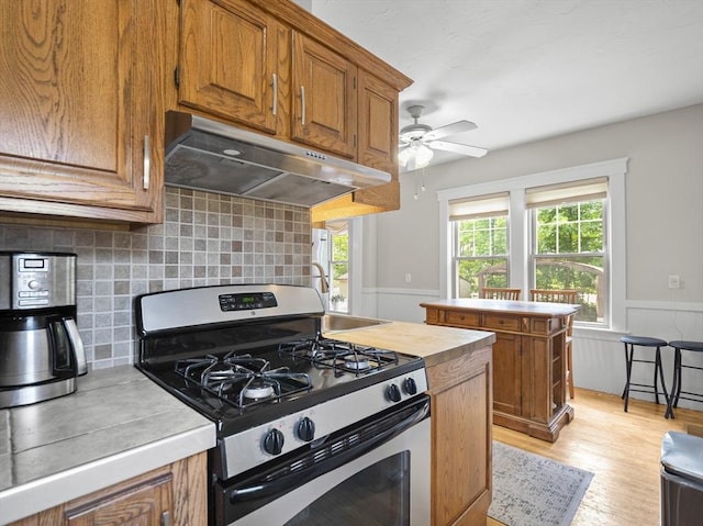 537 Milk St, Fitchburg, MA 01420 - kitchen with stainless steel gas range, under cabinet range hood, light countertops, wainscoting, and brown cabinets