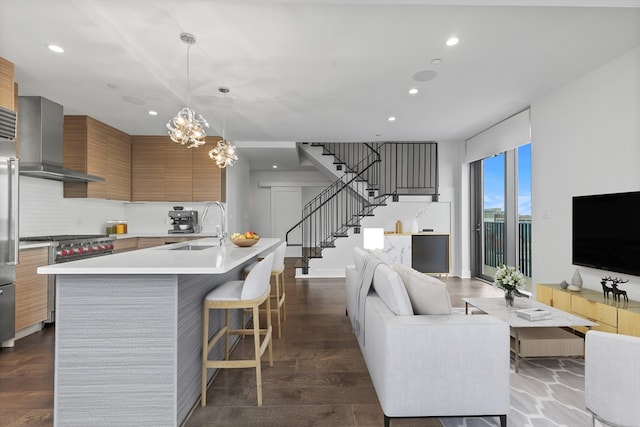 kitchen featuring a kitchen island with sink, wall chimney exhaust hood, a chandelier, and dark hardwood / wood-style flooring