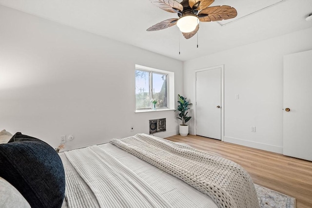 bedroom with light wood-style flooring, heating unit, baseboards, and ceiling fan