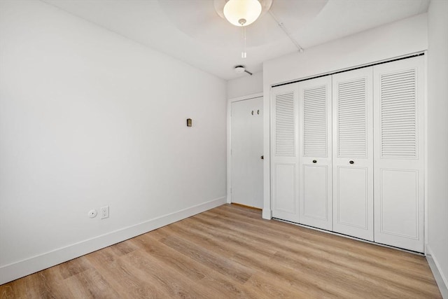 unfurnished bedroom featuring a closet, light wood-style flooring, a ceiling fan, and baseboards