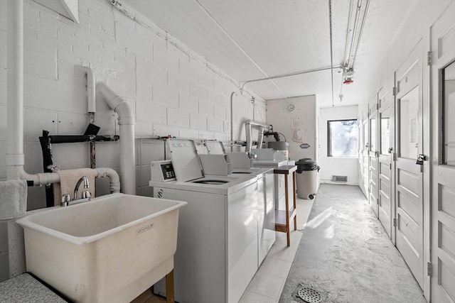 clothes washing area featuring washer and dryer, concrete block wall, visible vents, and a sink