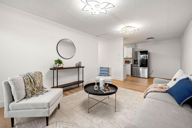 living area with baseboards, a textured ceiling, and light wood finished floors