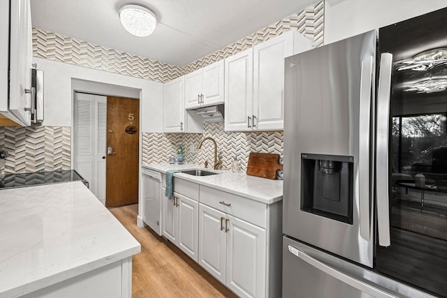 kitchen with white dishwasher, a sink, stainless steel fridge, light wood-type flooring, and backsplash