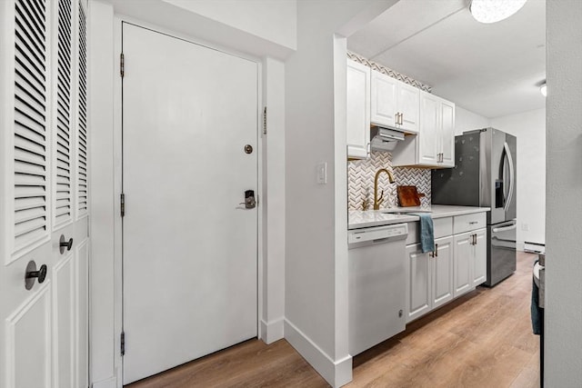 kitchen featuring light wood finished floors, stainless steel refrigerator with ice dispenser, tasteful backsplash, white dishwasher, and light countertops