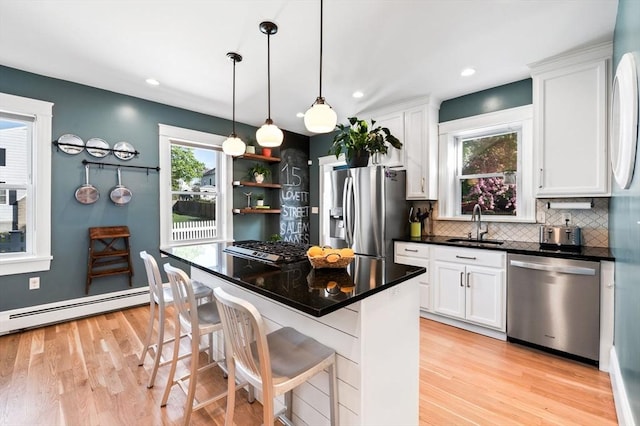 kitchen with appliances with stainless steel finishes, a sink, white cabinetry, decorative backsplash, and light wood-type flooring