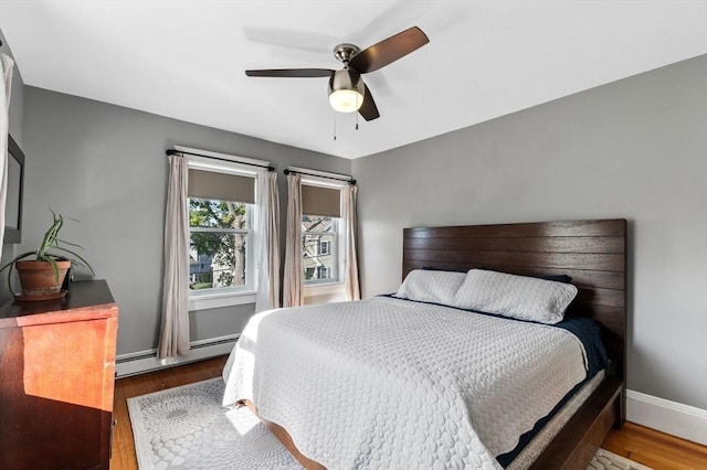 bedroom with ceiling fan, wood finished floors, baseboards, and a baseboard heating unit