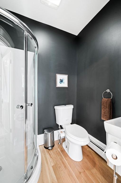 full bath with toilet, wood finished floors, baseboards, a shower stall, and a baseboard radiator