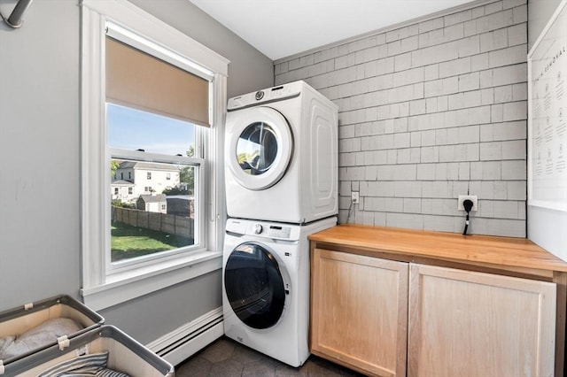 laundry room featuring a baseboard heating unit, stacked washing maching and dryer, cabinet space, and dark tile patterned floors