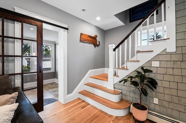 stairway featuring plenty of natural light, baseboards, baseboard heating, and wood finished floors