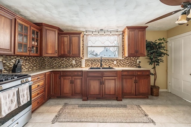 kitchen featuring a sink, light countertops, stainless steel range with gas cooktop, brown cabinets, and tasteful backsplash