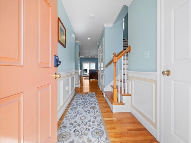 entryway with light wood finished floors, crown molding, stairs, wainscoting, and a decorative wall