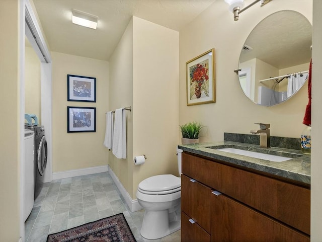 bathroom with vanity, toilet, washing machine and dryer, and baseboards