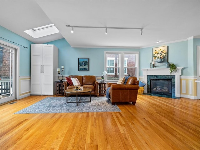 living room featuring ornamental molding, track lighting, a high end fireplace, vaulted ceiling with skylight, and light wood finished floors