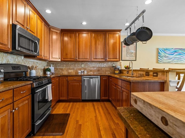 kitchen with light wood-style flooring, a sink, stainless steel appliances, brown cabinetry, and decorative backsplash