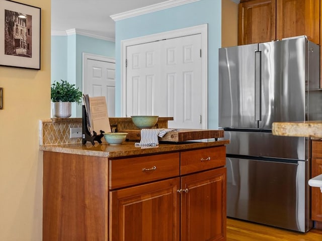 kitchen featuring brown cabinetry, light wood finished floors, crown molding, and freestanding refrigerator