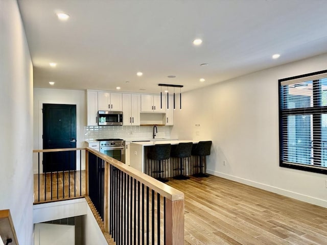 252 Main St Unit 101, Medford, MA 02155 - kitchen with appliances with stainless steel finishes, light countertops, white cabinetry, decorative backsplash, and light wood-type flooring