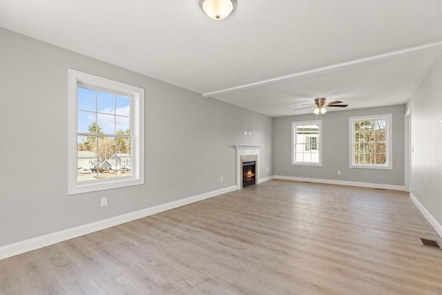 unfurnished living room with light wood finished floors, visible vents, ceiling fan, baseboards, and a lit fireplace
