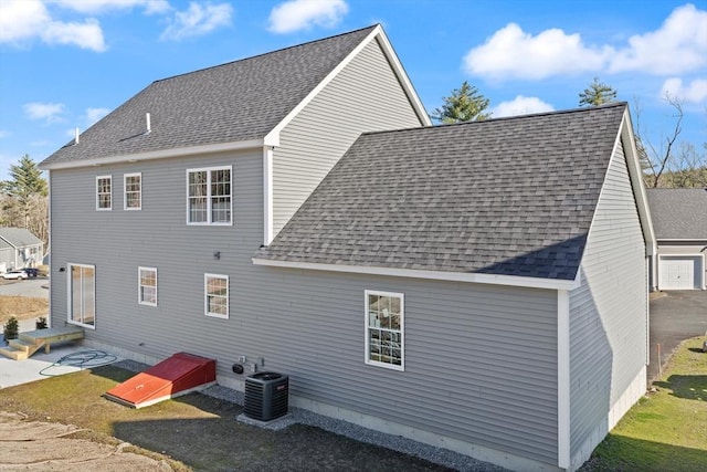 rear view of property featuring central AC unit and a shingled roof