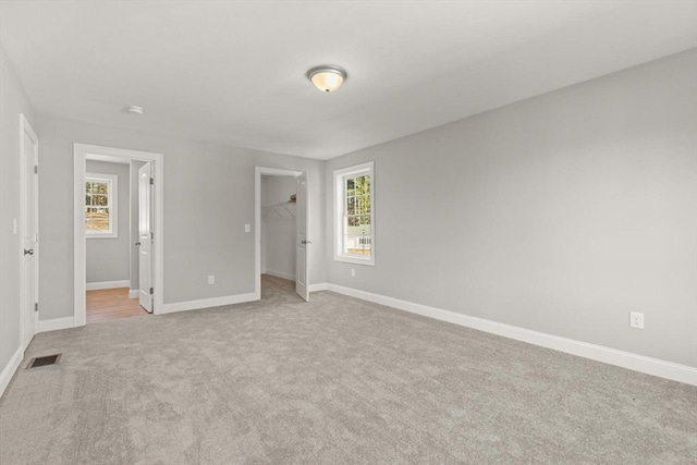 unfurnished bedroom with visible vents, baseboards, light colored carpet, and a spacious closet