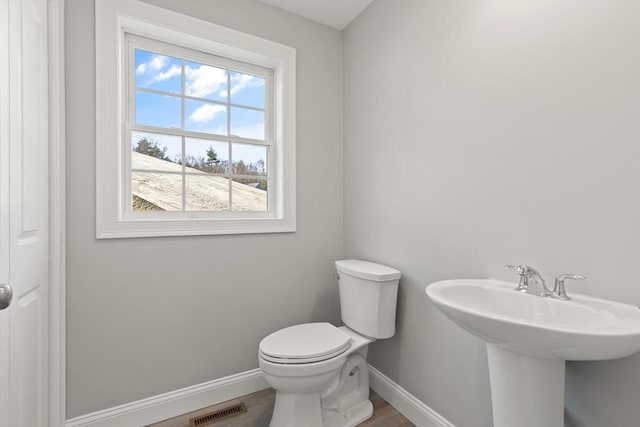 half bath with visible vents, baseboards, toilet, and wood finished floors