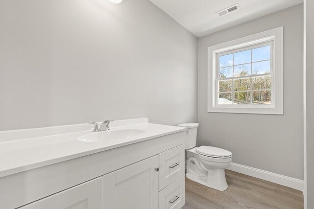 bathroom featuring visible vents, baseboards, toilet, wood finished floors, and vanity
