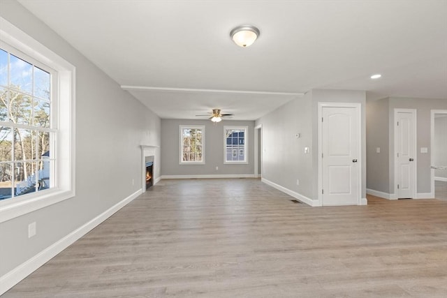 unfurnished living room with a ceiling fan, baseboards, light wood finished floors, and a healthy amount of sunlight