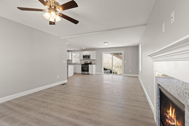unfurnished living room with light wood finished floors, a fireplace, a ceiling fan, and baseboards