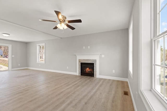 unfurnished living room featuring a wealth of natural light, visible vents, light wood-style floors, and ceiling fan