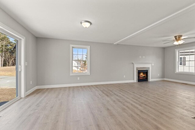 unfurnished living room featuring light wood-style flooring, a warm lit fireplace, a ceiling fan, and baseboards
