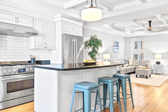 49 Baldwin St Unit 1, Boston, MA 02129 - kitchen with stainless steel appliances, under cabinet range hood, coffered ceiling, dark countertops, and a kitchen bar