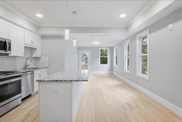 kitchen with a center island, pendant lighting, stainless steel appliances, white cabinets, and light stone countertops