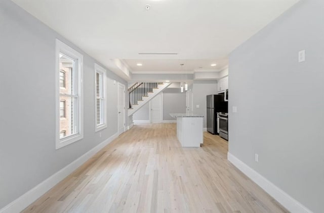 unfurnished living room with recessed lighting, light wood-style flooring, baseboards, and stairs