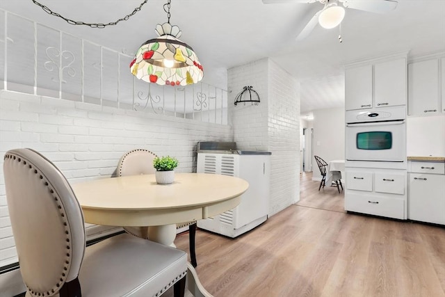 dining space with ceiling fan, brick wall, and light hardwood / wood-style flooring