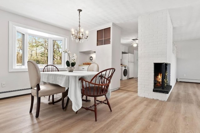 dining space with washer / clothes dryer, light hardwood / wood-style flooring, a brick fireplace, and baseboard heating