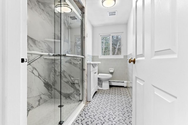 bathroom featuring baseboard heating, tile walls, vanity, a shower with shower door, and toilet