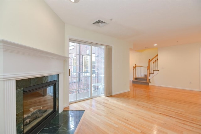 unfurnished living room featuring a premium fireplace, baseboards, wood finished floors, visible vents, and stairway