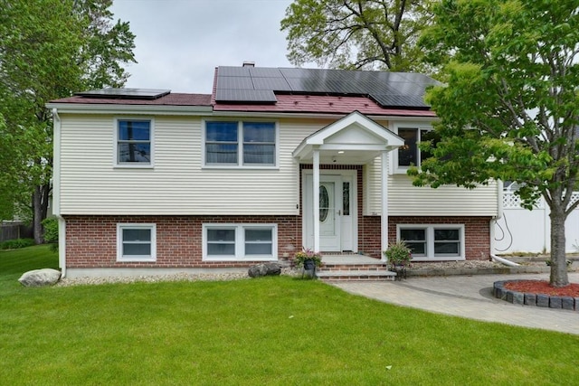split foyer home with a front lawn, solar panels, and brick siding