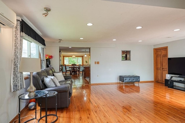 living room featuring a wall mounted AC, light wood finished floors, recessed lighting, and baseboards