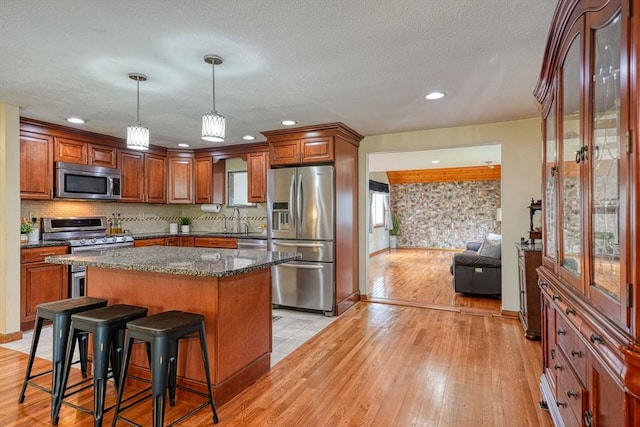 kitchen with appliances with stainless steel finishes, a kitchen bar, light wood-style floors, brown cabinetry, and a kitchen island