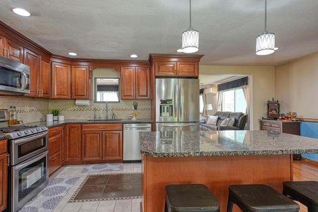 kitchen with appliances with stainless steel finishes, a sink, decorative backsplash, a kitchen breakfast bar, and healthy amount of natural light