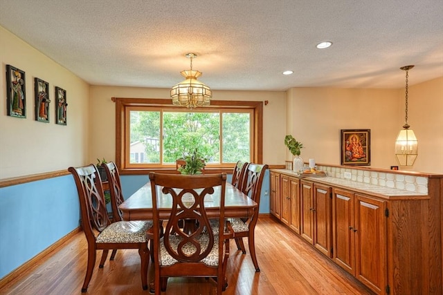 dining space featuring light wood-style floors, a textured ceiling, baseboards, a chandelier, and recessed lighting