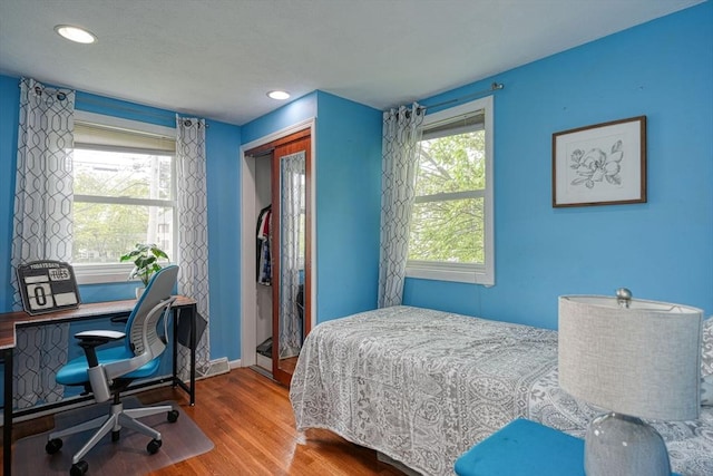 bedroom featuring wood finished floors, a closet, an office area, baseboards, and recessed lighting