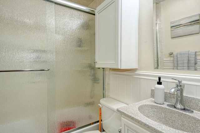 full bathroom with an enclosed shower, vanity, a wainscoted wall, and toilet