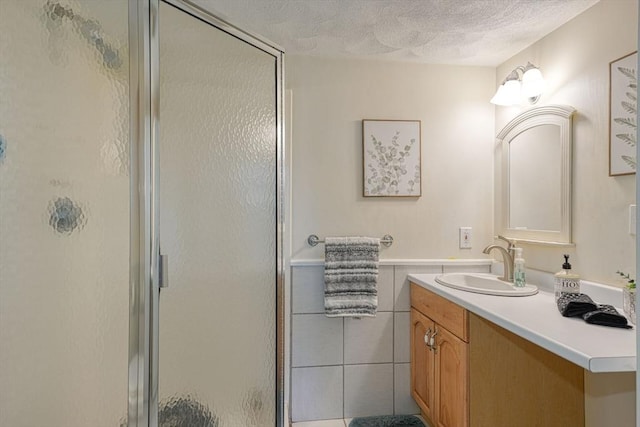 full bath with a shower stall, a textured ceiling, vanity, and tile walls