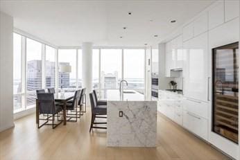 kitchen featuring floor to ceiling windows, a kitchen island with sink, light wood-style flooring, and modern cabinets