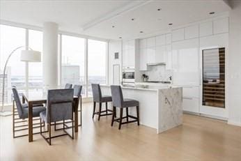 kitchen with light wood-style flooring, a breakfast bar, white cabinetry, floor to ceiling windows, and modern cabinets