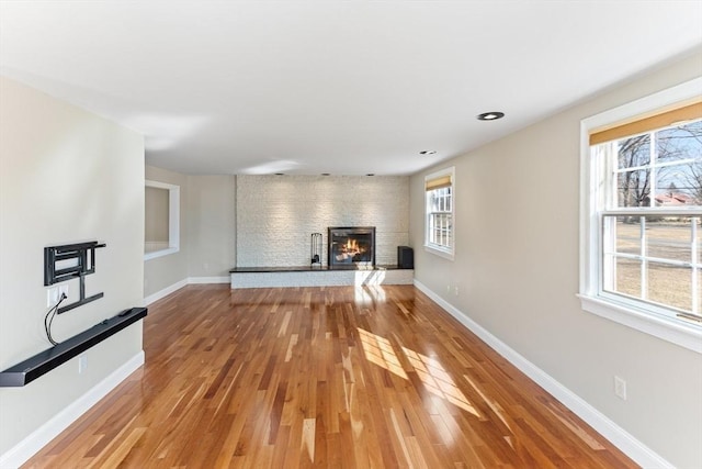 unfurnished living room featuring light wood finished floors, a brick fireplace, and baseboards