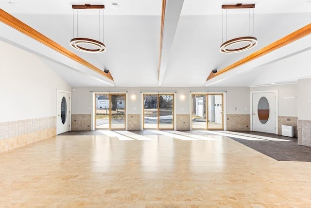 unfurnished living room featuring a chandelier, a wainscoted wall, lofted ceiling with beams, french doors, and wood finished floors
